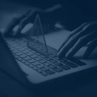 Hands typing on a laptop keyboard with a digital warning symbol, emphasizing security updates for electrotechnology training.